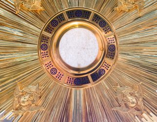 A gold sunburst on a pole with a clock in the background