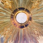 A gold sunburst on a pole with a clock in the background